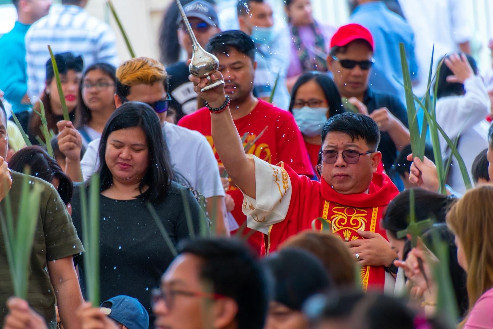 A priest in red robes blesses a crowd during a vibrant outdoor religious ceremony.