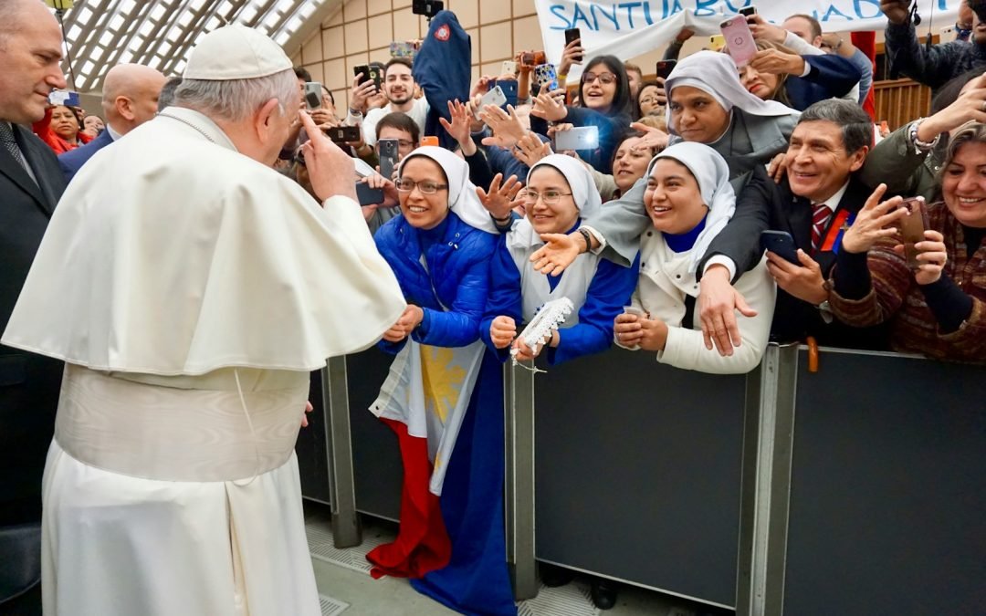 Pope Francis standing surrounded with people