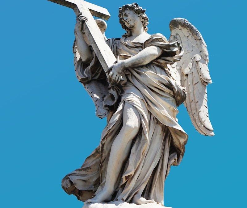 angel holding cross statue during day