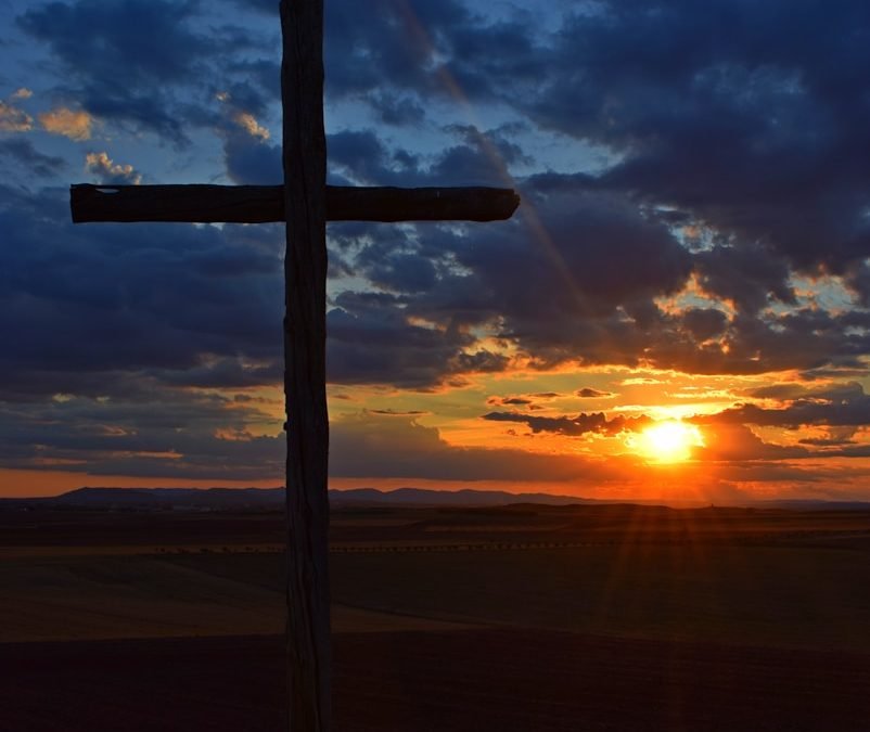 a cross on a hill with a sunset in the background